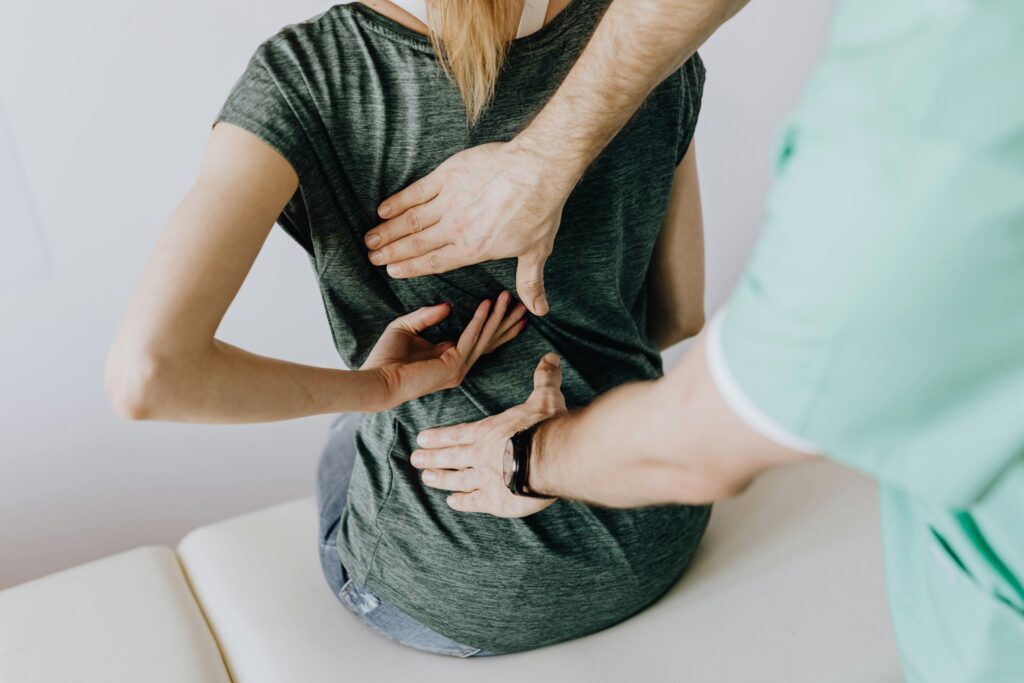 Medical professional assessing a patient's back pain during a physical examination, with hands placed on the spine area.