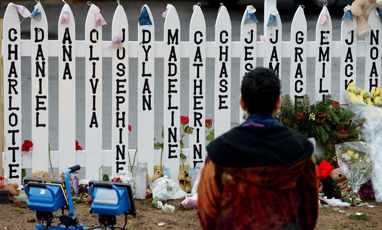 Woman at Sandy Hook Elementary School Shooting Memorial with names and ribbons on fence posts