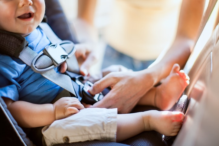 A mother buckles the car seat harness for an infant boy.