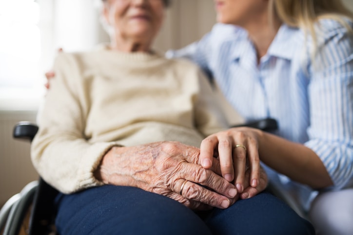 A closeup of a woman's aged hands is shown with her daughter's hand over them. Elder abuse is best prevented by close and caring relationships.