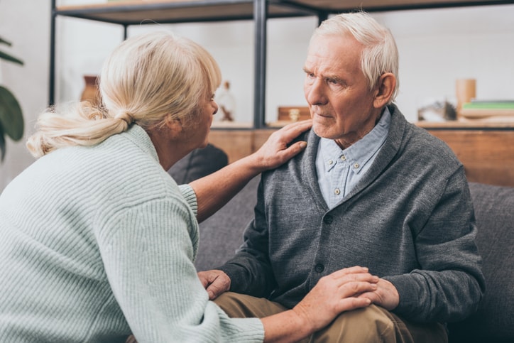 A middle aged light haired woman bends down to speak with her seated elderly father. Victims are not always able to speak up about elder abuse.