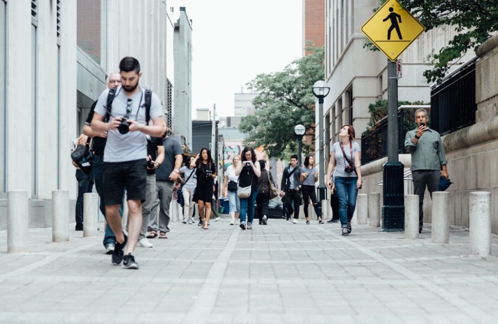 A busy sidewalk shows pedestrians on their phones, distracted and talking as they walk. Pedestrian safety is the responsibility of both the pedestrian and driver.