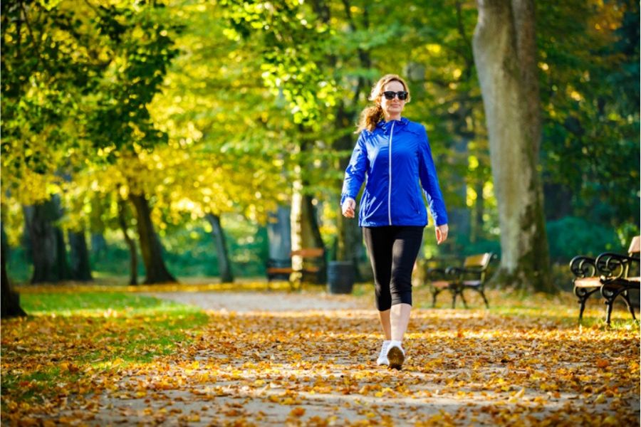 A woman takes a brisk walk down a leafy path of a park. She shows recovery following a concussion from a car accident.