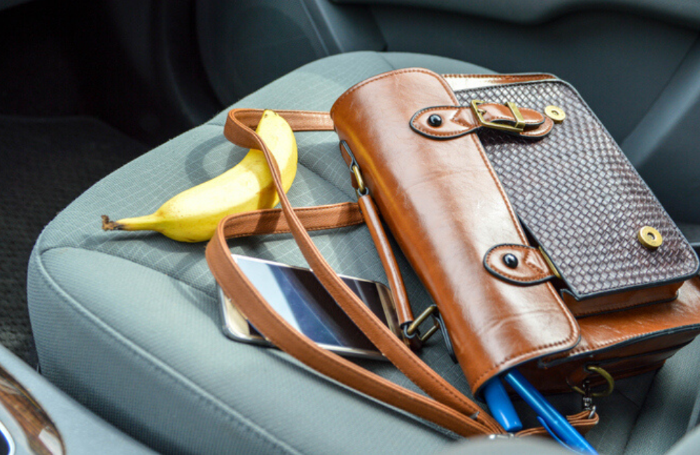 A brown purse with a banana and cell phone sit piled onto a passenger seat in a car. Help prevent distracted driving by putting cell phones out of reach.