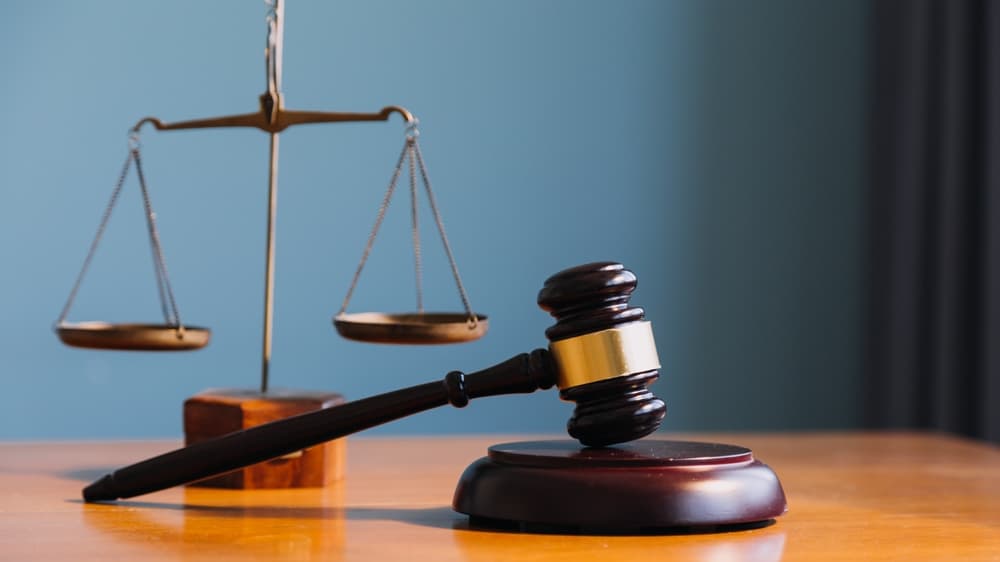 Judge’s gavel resting on a wooden table with scales of justice in the background.