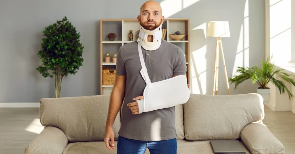 injured man with neck brace and arm sling standing in living room