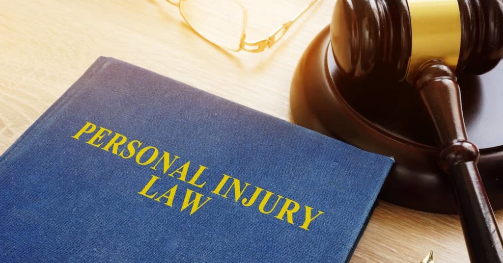 book titled Personal Injury Law on a table next to a gavel and reading glasses