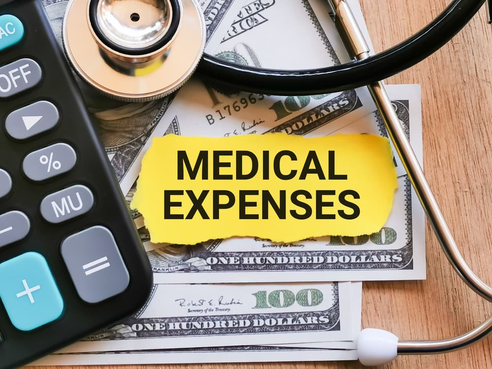 The phrase "MEDICAL EXPENSES" written on a paper strip alongside a stethoscope, calculator, and money—symbolizing healthcare costs and financial planning.