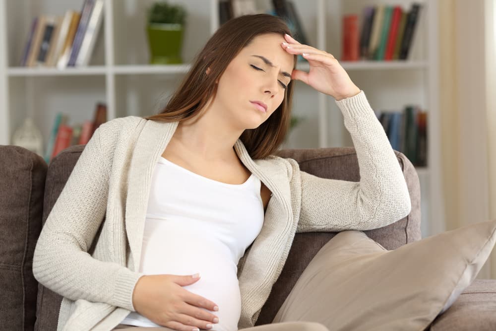 Pregnant woman on home sofa experiencing a migraine.