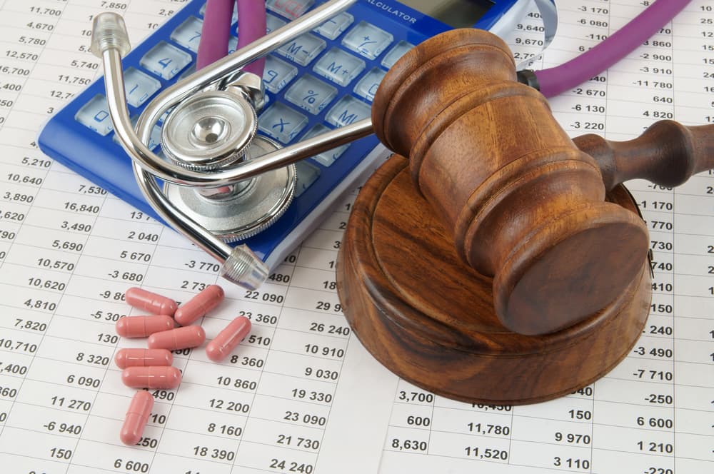 Gavel, stethoscope, and pills atop a financial document, symbolizing the intersection of legal and medical aspects in healthcare finance.