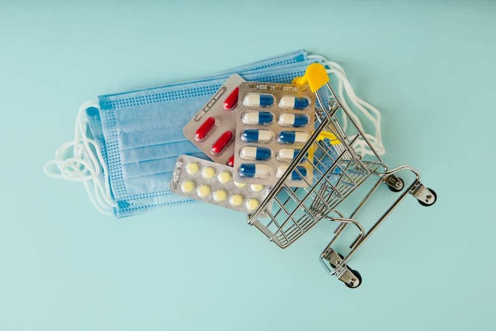 Shopping cart with pills and stack of masks, symbolizing the intersection of medicine and the sale of pharmaceuticals.