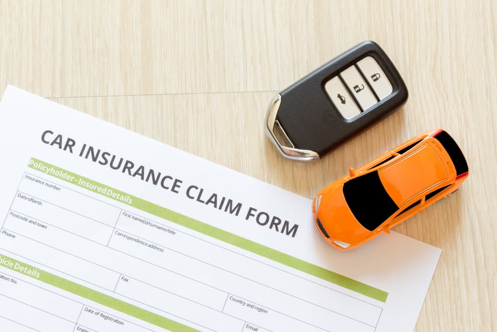 Aerial perspective of an car insurance claim form placed on a wooden desk, accompanied by a car key and a toy car.