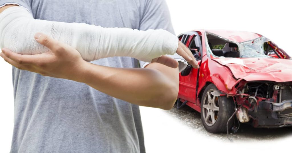 injured man with broken arm standing in front of wrecked car