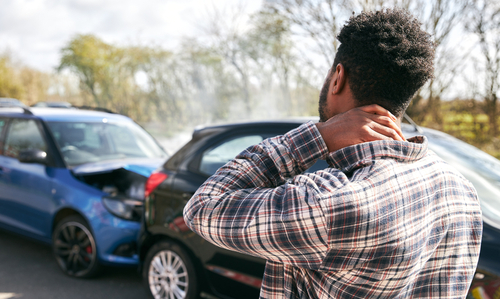 Man holding his neck in pain after a rear-end car accident involving two vehicles on a road.