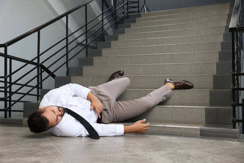 Man in business attire lying injured on stairs after a slip and fall accident indoors.