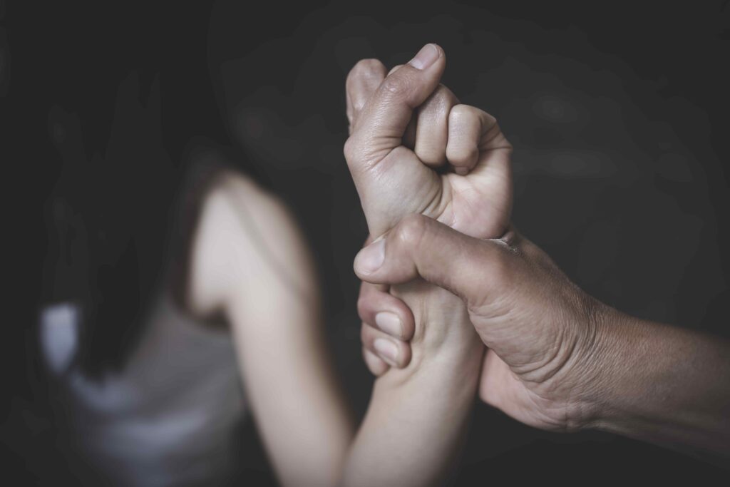 Close-up of domestic violence concept showing a hand gripping a woman’s wrist tightly.