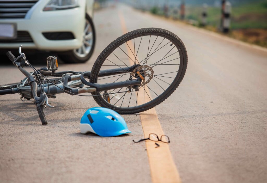 Bicycle accident scene with car, fallen bike, helmet, and broken glasses on road.