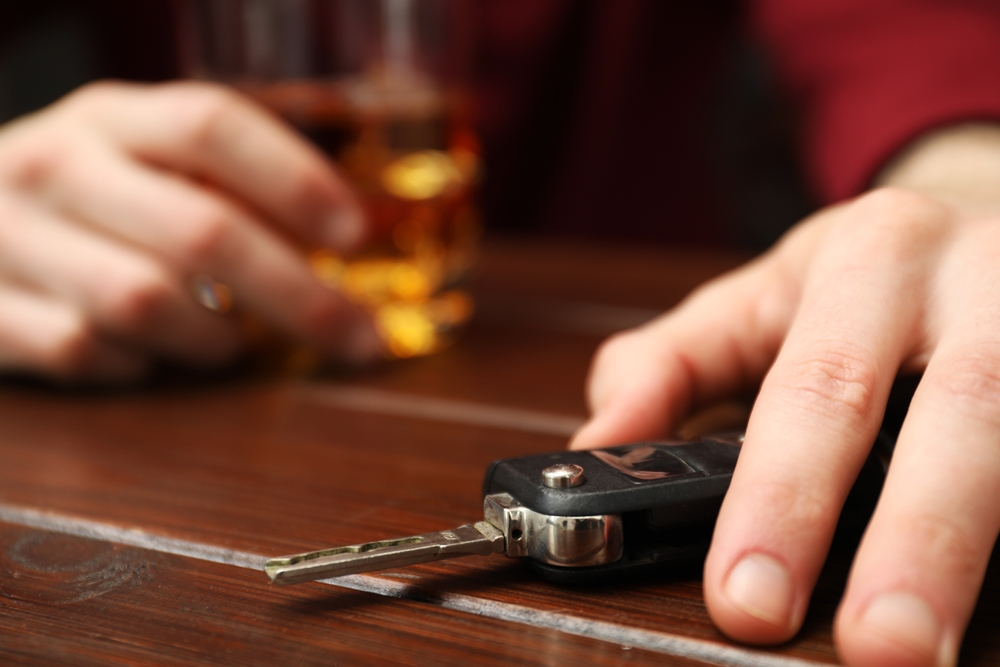A person holding a glass of alcohol while reaching for car keys, highlighting the moment where the risks of DUI accidents often begin.