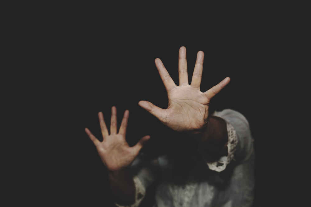 A person raises both hands defensively in a dark setting, capturing the fear and trauma often discussed with a Danbury Sexual Assault Lawyer.