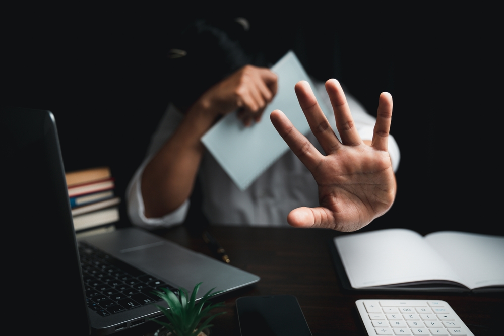 Waterbury Sexual Assault Lawyer supporting a person covering their face while raising a hand in distress at a desk with a laptop and books.