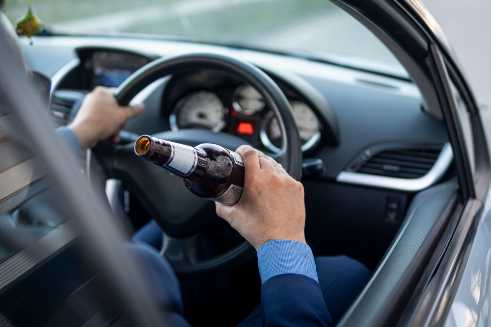 A driver holding a beer bottle while operating a car, illustrating the dangerous behavior often reviewed by a Glastonbury drunk driving accident lawyer.