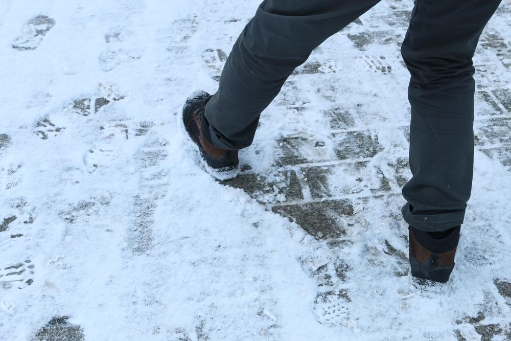 Close-up of man's feet slipping on snowy sidewalk